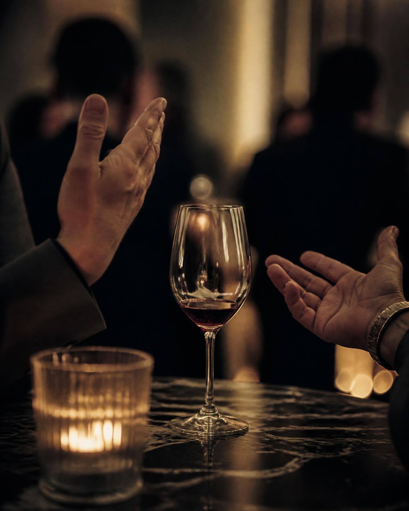 Detalhe de uma conversa à mesa, copo de vinho e luz de vela