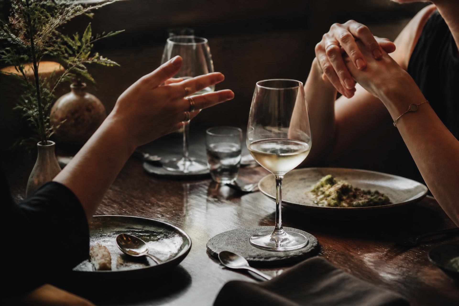 Mãos de duas mulheres em conversa sobre uma mesa posta, luz natural quente